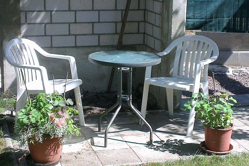 Grau möblierte Terrasse mit Tisch, Stühlen und Blumentopf im Garten.