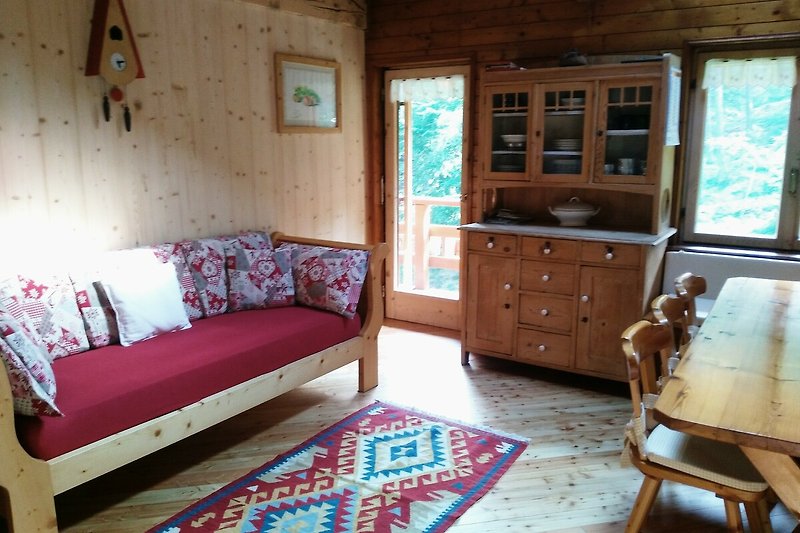 Gemütliches Wohnzimmer mit Holzmöbeln und Fensterblick und Zugang auf den Balkon