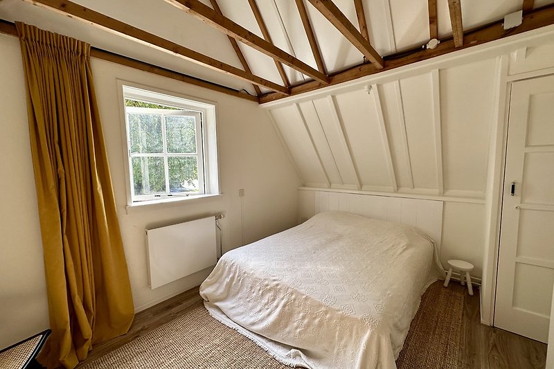 Gemütliches Schlafzimmer mit Holzboden, Vorhängen und bequemem Bett.