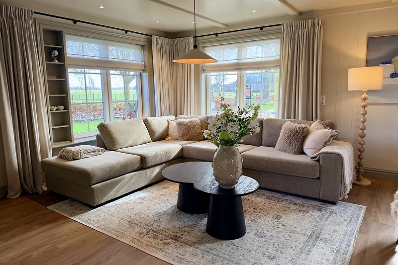 Großzügiger Wohnbereich mit Sofa, Esstisch, Lampen und Fensterdeko.