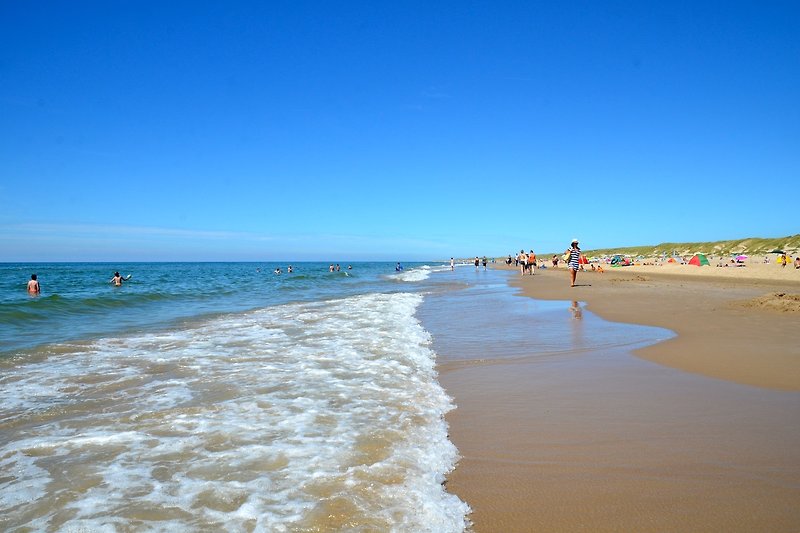 Schöner Strand mit blauem Wasser, weißem Sand und entspannten Menschen. Perfekt für einen erholsamen Urlaub am Meer.