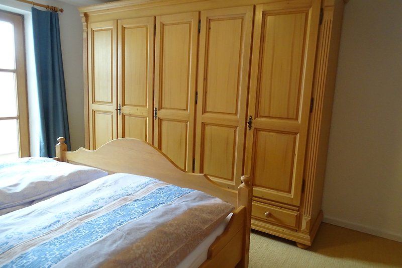 Gemütliches Schlafzimmer mit Holzbett, Vorhängen und Holzboden.