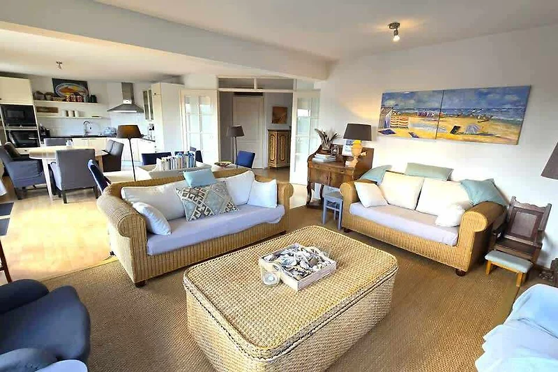 Großzügiges Wohnzimmer mit Sofa, Sessel, Couchtisch und Zimmerpflanze.