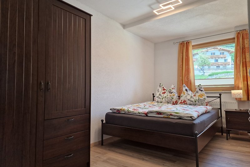 Gemütliches Schlafzimmer mit Holzmöbeln, bequemem Bett und Fensterbehang.