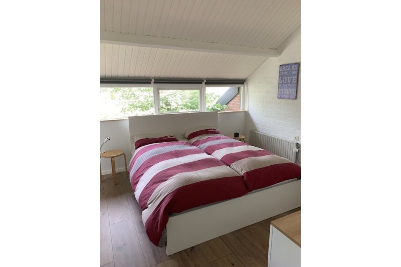 Gemütliches Schlafzimmer mit Holzboden und gemusterten Bettwäsche. Holz, Komfort, Bett, Fenster.