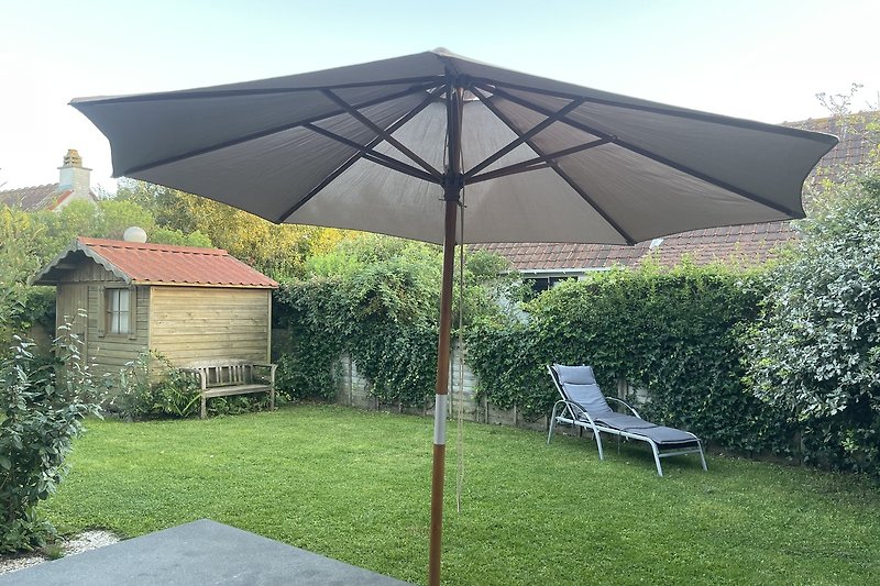 Ein sonniger Garten mit einem Schirm, Tisch und Stühlen.