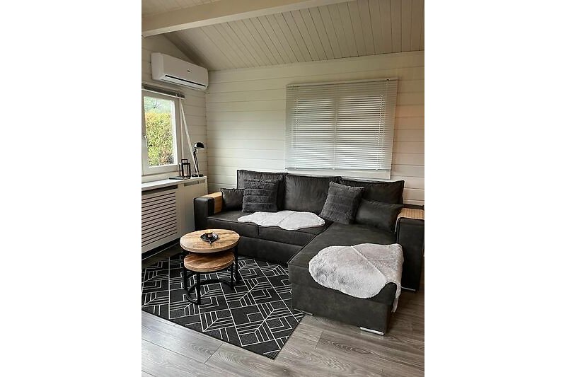 Gemütliches Wohnzimmer mit bequemer Couch, Holzmöbeln und Fensterblenden.