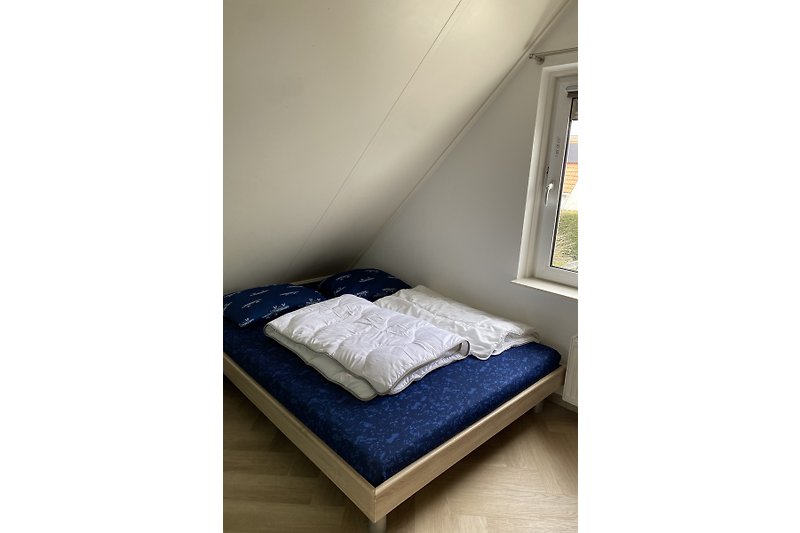 Gemütliches Schlafzimmer mit Holzboden, Fenster und gemusterten Bettwäsche.