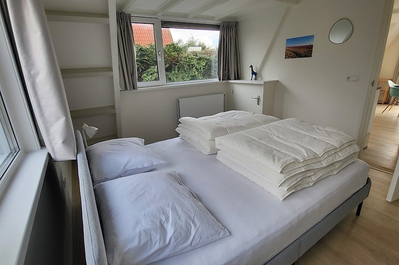Modernes Schlafzimmer mit bequemem Bett, Holzmöbeln und Pflanze.