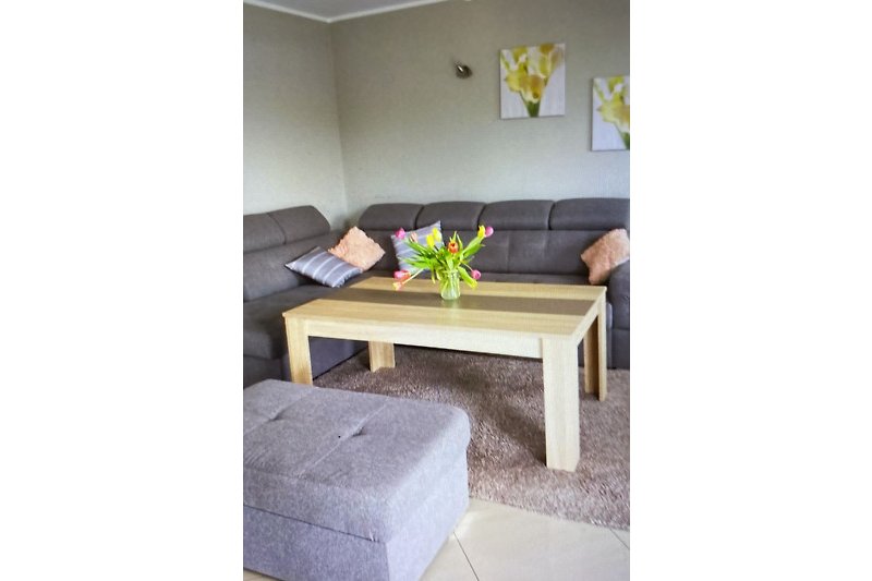 Wohnzimmer mit lila Sofa, Holztisch und Blumendekoration.