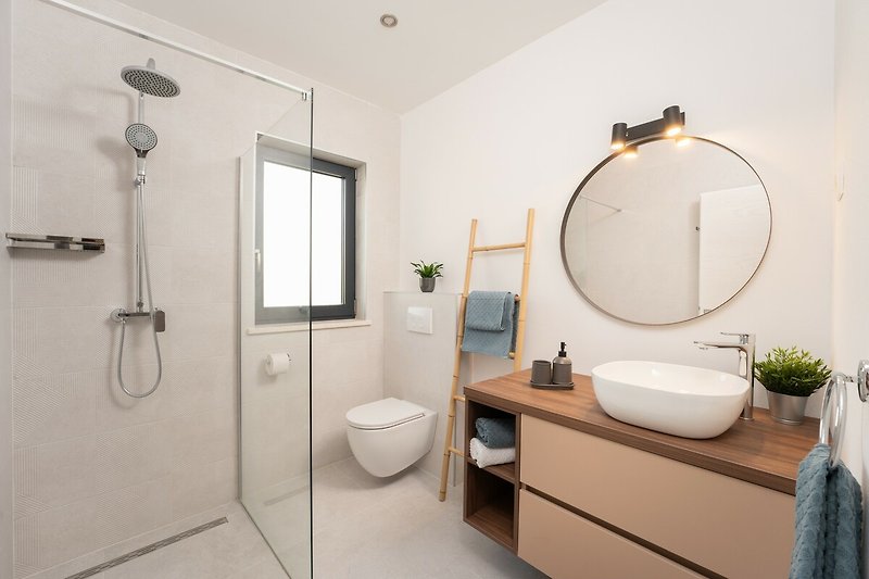 Modernes Badezimmer mit Dusche, Spiegel und Pflanze.
