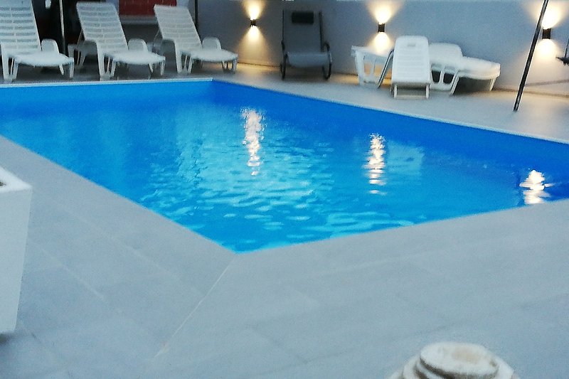 Schwimmbad mit Holzboden und Außenmöbeln in einem Ferienort.