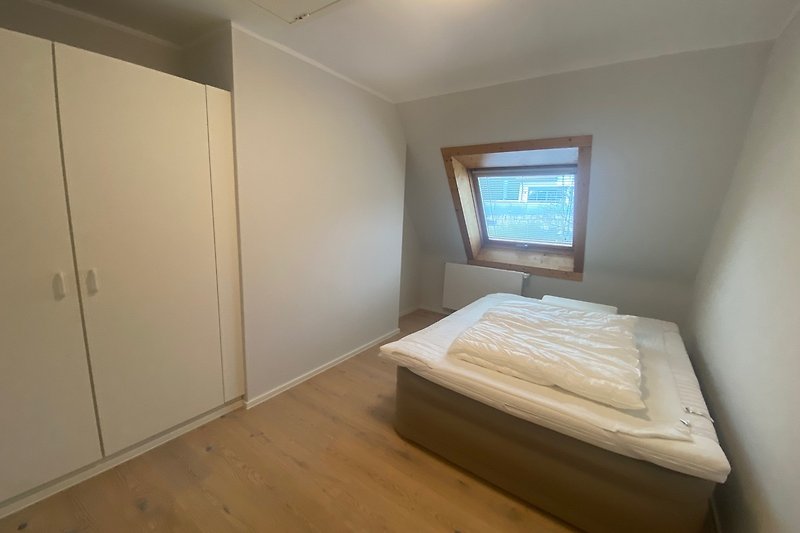 Gemütliches Schlafzimmer mit Holzbett, Fernseher und Fenster.