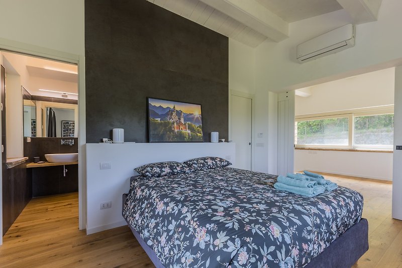 Schlafzimmer mit Bett, Kissen, Holzbalken und Fensterblick.