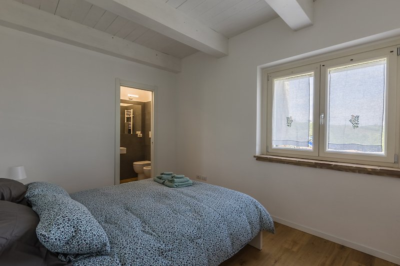 Geräumiges Schlafzimmer mit Holzbalken, Bett und Fensterblick.