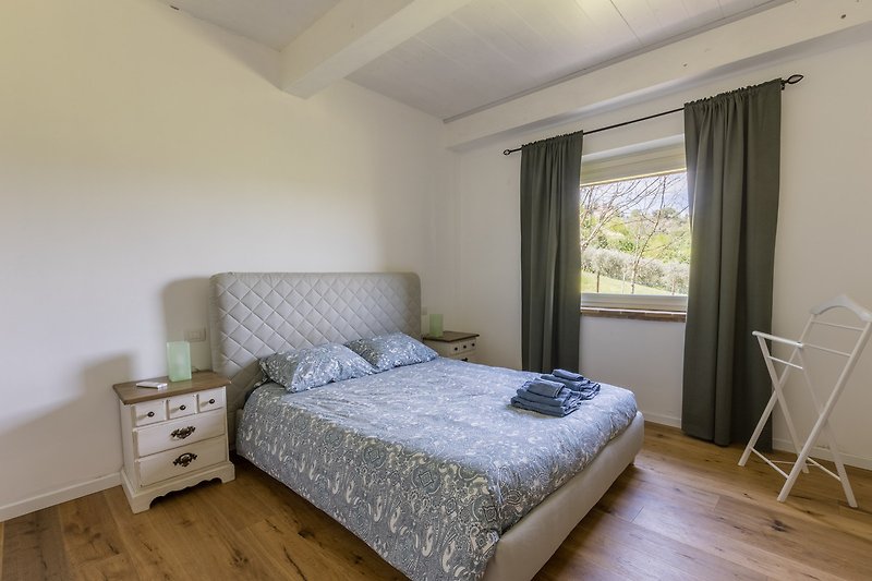 Gemütliches Schlafzimmer mit Bett, Kissen, Fensterblick und Holzmöbeln.
