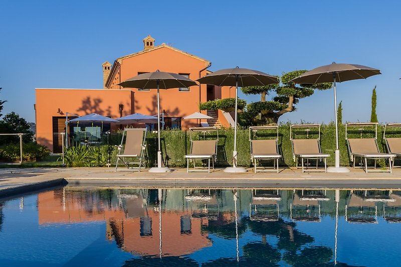 Una vista mozzafiato sulla piscina e il paesaggio collinare di una casa vacanza con arredi esterni.
