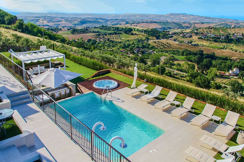 Pool mit Liegestühlen, umgeben von Palmen und blauem Himmel.