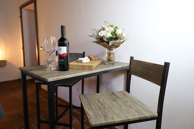 Tavolo, sedia, bottiglia di vino, fiori e lampada in una stanza.