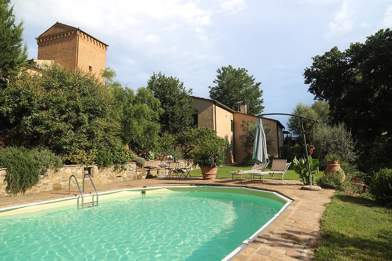Ein Schwimmbad mit einem Garten, Bäumen und einem blauen Himmel.