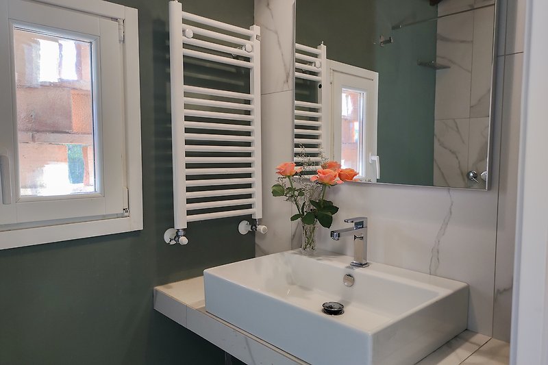 Affitto di una casa con specchio, rubinetto e fiori in bagno.