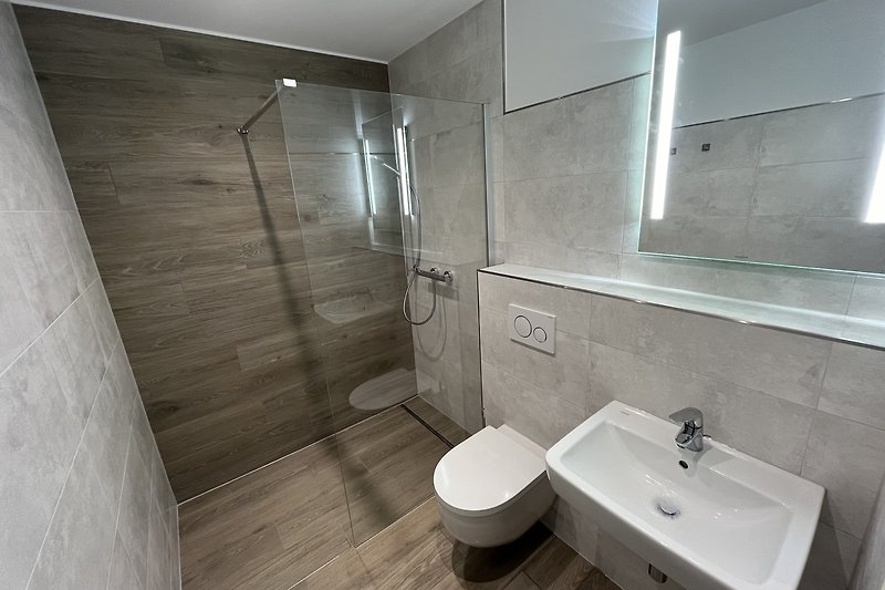 Badezimmer mit Spiegel, Waschbecken und ebenerdiger Dusche.