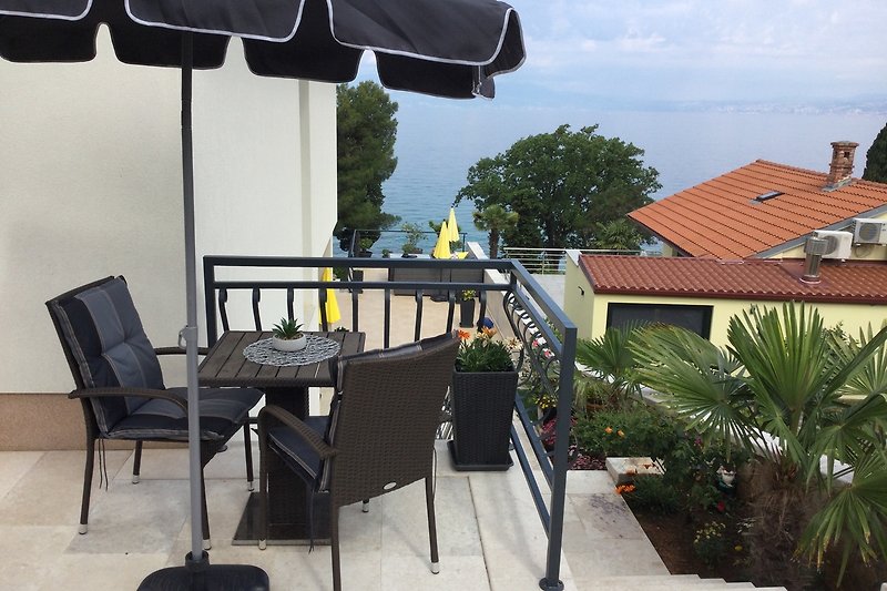 ELI- Balkon mit Outdoor-Möbeln, Sonnenschirm und Pflanzen. Gemütliche Atmosphäre. blick zum Meer