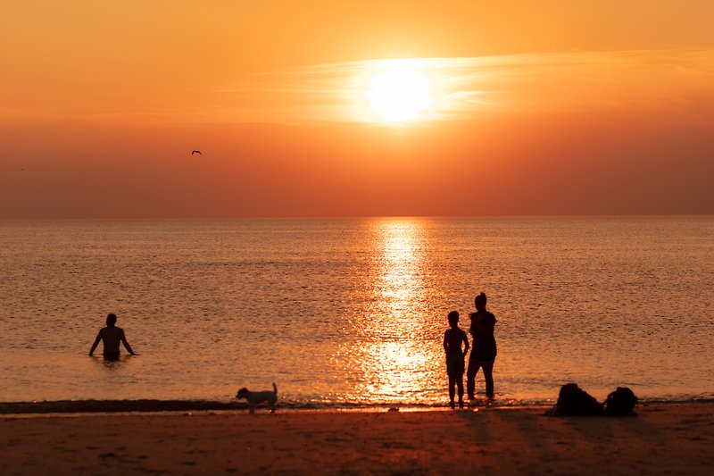 Sonnenuntergang am Strand mit spielenden Kindern und sanften Wellen.