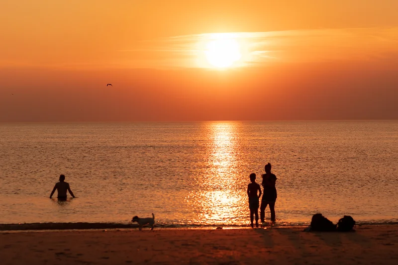 Sonnenuntergang am Strand mit spielenden Kindern und sanften Wellen.