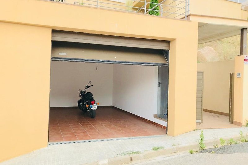 Modernes Haus mit Garage, Motorrad und Auto auf Asphalt.