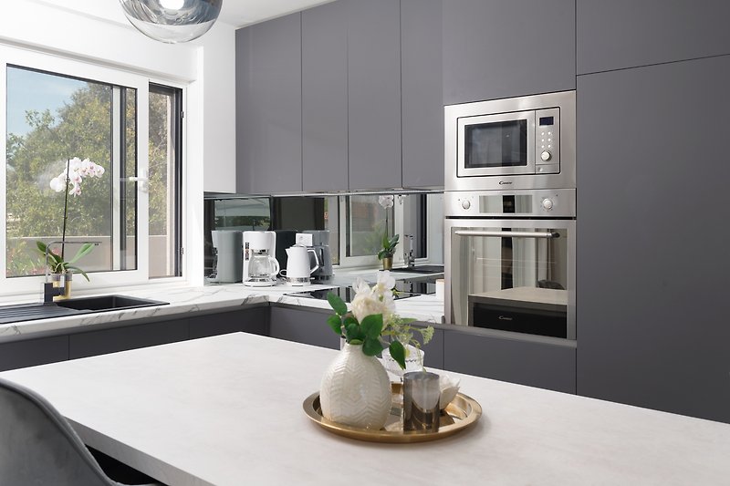 Moderne Küche mit weißer Arbeitsplatte, grauen Schränken und Holzboden.