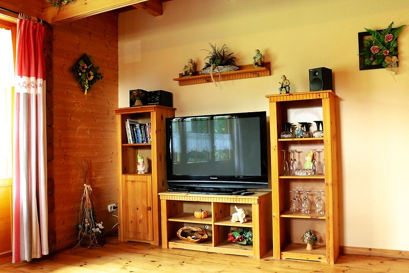 Gemütliches Wohnzimmer mit Holzmöbeln, Bücherregal und Pflanzen.
