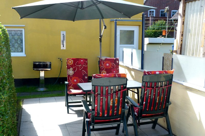 Außenbereich mit Tisch, Stühlen, Sonnenschirm und Grill.