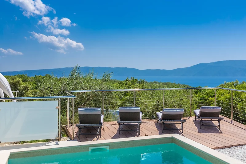 Pool mit Sonnenliegen, Schirmen und Blick auf tropische Bucht.