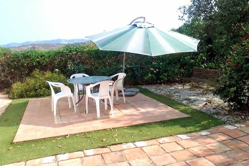 Ein sonniger Garten mit Tisch, Stühlen und Schatten.