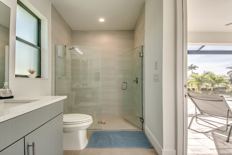 Modernes Badezimmer mit Spiegel, Pflanze, Waschbecken und Dusche.