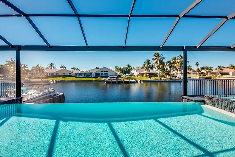 Pool mit Palmen, Wasserlandschaft und schattigen Relaxbereichen.