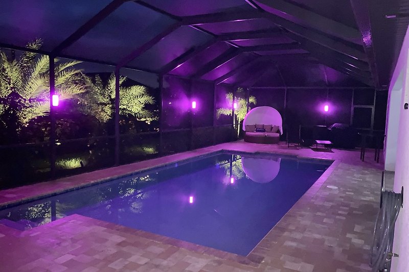 Modernes Ferienhaus mit lila Pool und exotischer Gartenlandschaft.