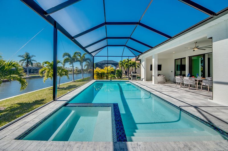 Luxuriöses Schwimmbad mit Sonnenliegen und Palmen.