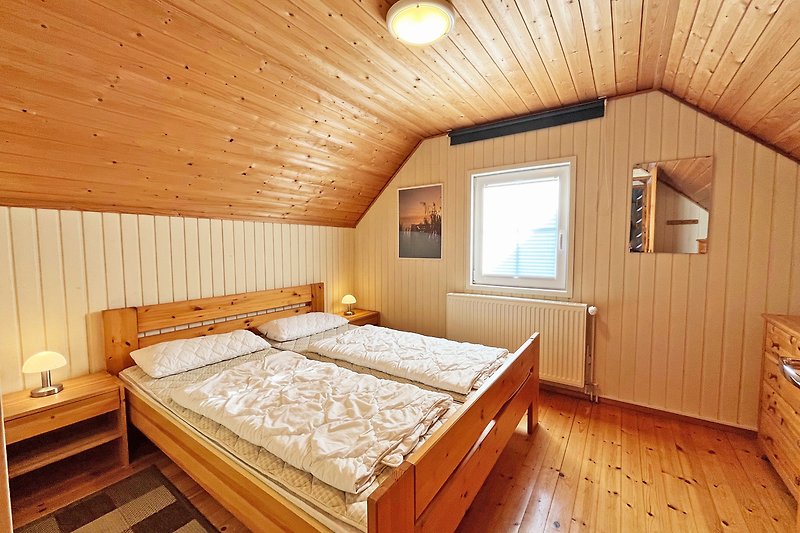 Schlafzimmer 2 mit gemütlichem Bett, TV, Holzmöbeln und Fensterblick.