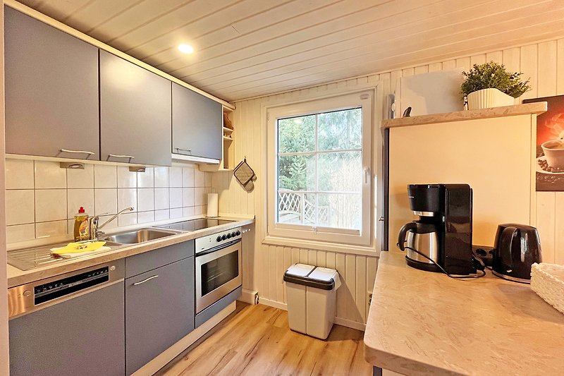 Küche mit Holzfronten, Spülbecken, Herd und Fenster.