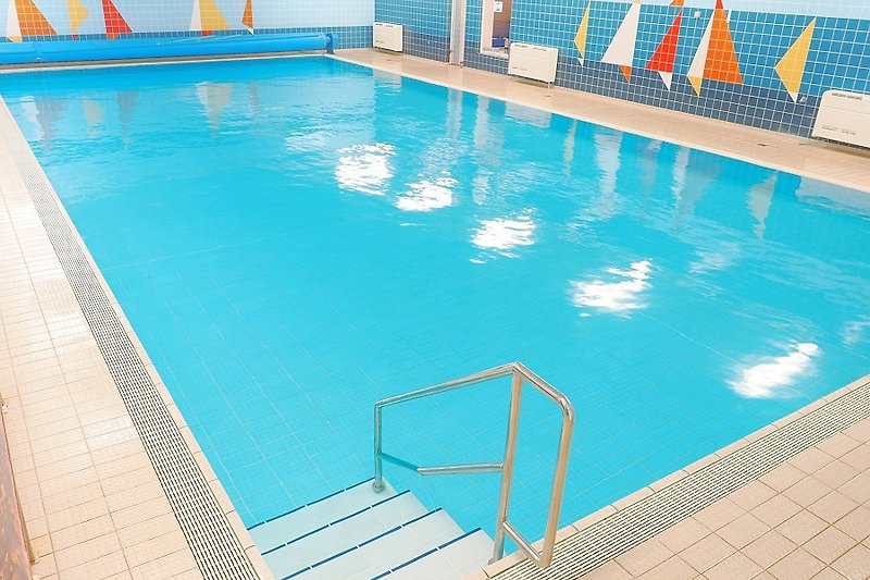 Schwimmbad mit blauem Wasser und Außenmöbeln in einem rechteckigen Gebäude.