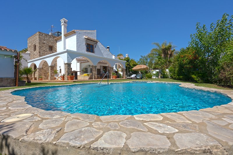 Luxuriöse Villa mit Pool, umgeben von üppiger Natur und klarem Himmel.