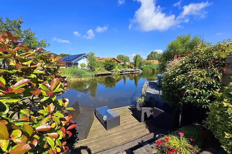 Haus am Wasser mit Garten und Teich, umgeben von Natur.