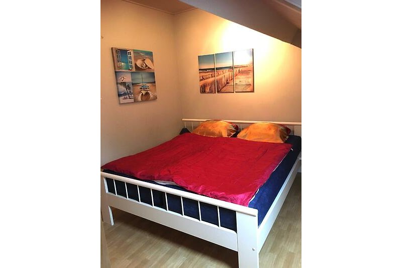Schlafzimmer mit Holzbett, Kissen, Bettwäsche und Kunst.