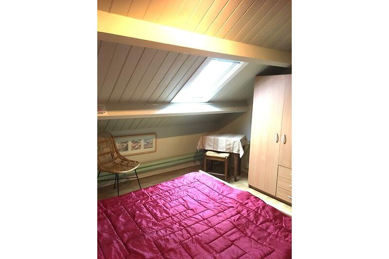 Schlafzimmer mit Bett, Kissen, Decke und Holzdecke.