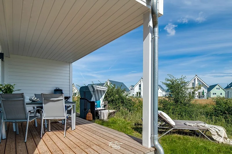 Terrasse en bois avec une table et des chaises sous un parasol, entourée de plantes vertes et de fleurs, offrant un espace agréable pour se détendre en plein air.