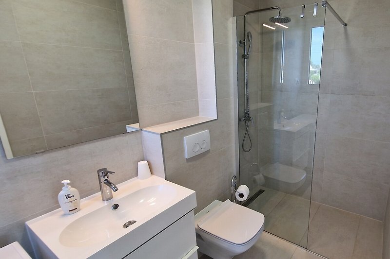 This modern bathroom features a sleek sink, mirror, and shower, providing a refreshing and luxurious experience for holidaymakers.