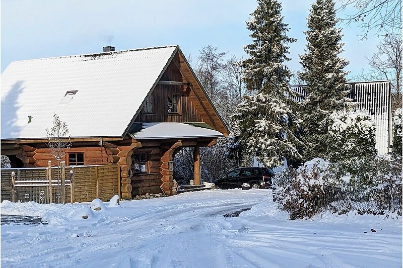 Winterliches Blockhaus mit verschneitem Dach und malerischer Landschaft. Perfekt für den Winter- und Sommerurlaub