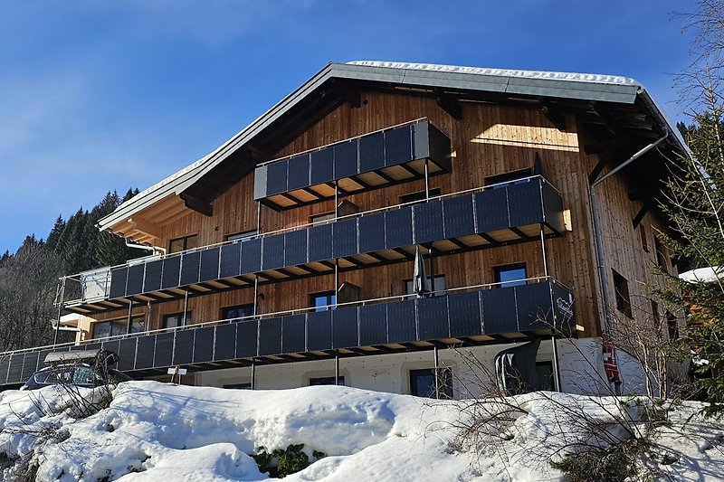 Gemütliches Haus mit Holzfassade, Fenstern und verschneitem Bergblick.